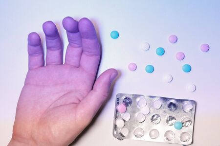 Blue male hand and randomly lying pills. The concept of drug overdose, the danger of poisoning, the method of suicide, a social problem.の写真素材