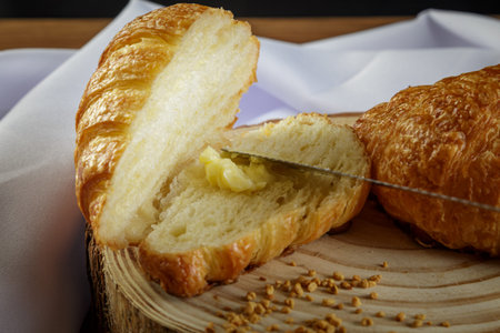 Delicious croissants on wooden trunk, with white towel around and buttering the sliced croissant -...