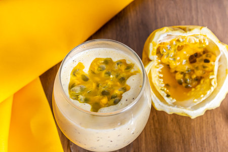 Passion fruit mousse in a glass bowl, with passion fruit in the background, on a wooden table and a yellow tablecloth around it. Close view.の写真素材
