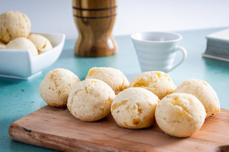 Delicious cheese bread, typical Brazilian dish, on a wooden board and table with a green background and white wall. Next to a cup of coffee.の写真素材