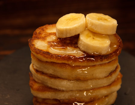 freshly baked pancakes stacked with banana pieces and dried with syrup