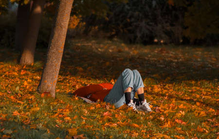 man rests lying on the grass strewn with yellow leaves in the parkの写真素材