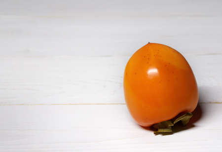 ripe, juicy orange persimmon on a white wooden tableの写真素材