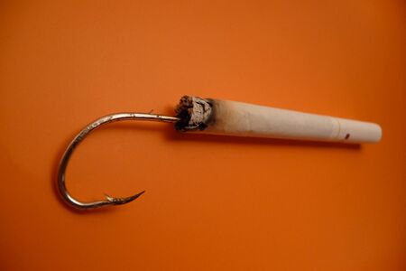 Fishing hook attached to a cigarette in a orange backgroundの写真素材