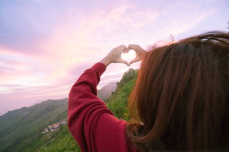 Hand of a young woman making a heart-shaped hands. To give love to each other with a view of nature. During the evening, and that makes it pretty light, its impact on the clouds.の写真素材