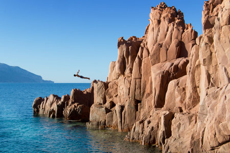 diver jumps from red rock in Arbatax Sardiniaの写真素材