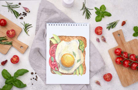 Watercolor illustration on page of notebook on the table on background of ingridienst for cooking meal. Fried egg toast with avocado, tomato and leaves of basilicum. Flatlay.の写真素材