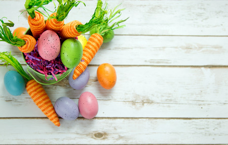 Whimsical Carrots and Easter Eggs in a pastel basket on a wood plank background board with room for copy spaceの写真素材
