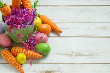 Orange striped faked carrots and colorful Easter Eggs on a rustic whitewashed wood background with room for textの写真素材