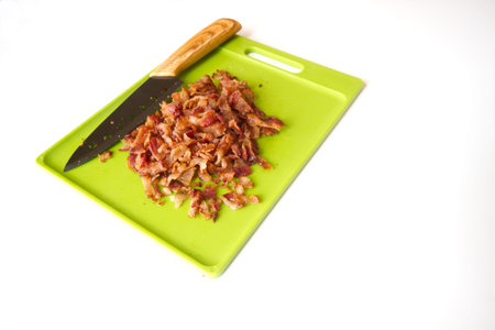Chopped Bacon on a green cutting board with a carving knife isolated on white background with room...