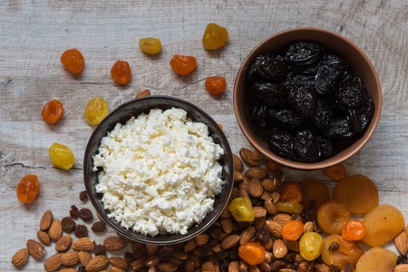 cottage cheese in white plate and the prunes in the brown plate. Prunes, dried apricots, dried mandarins and almonds on a light wooden background.の写真素材