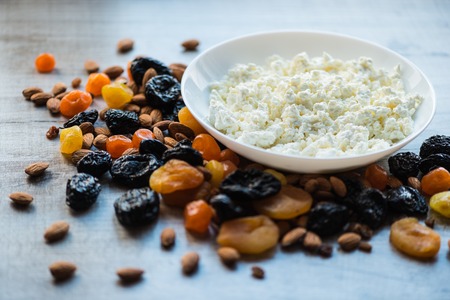 cottage cheese in white dish. Prunes, dried apricots, dried mandarins and almonds on a light wooden background.の写真素材