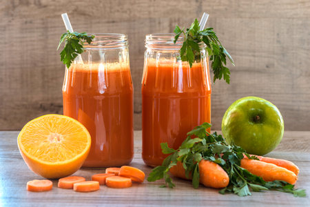 Fresh carrot juice in bottles on a grey wooden table.