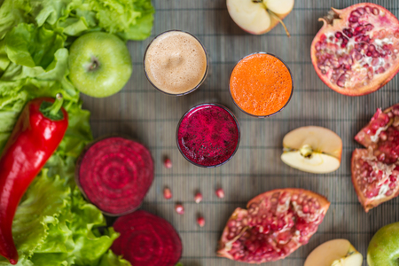 three glasses of different fresh juice. Beet, carrot and apple juices on grey wood backgroundの写真素材
