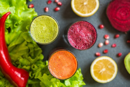 three glasses of different fresh juice. Beet, carrot and kiwi juices on grey backgroundの写真素材
