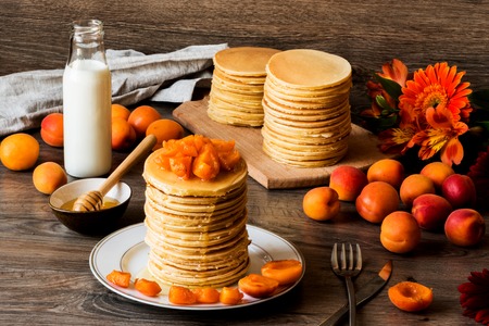 Stack of homemade american pancakes served with honey and apricots on wooden backgroundの写真素材