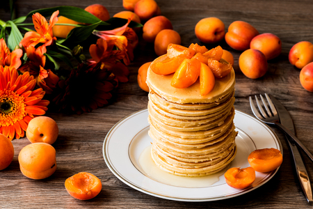 Stack of homemade american pancakes served with honey and apricots on wooden backgroundの写真素材