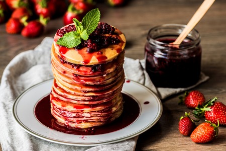 Stack of homemade american pancakes served with jam and strawberries on wooden backgroundの写真素材