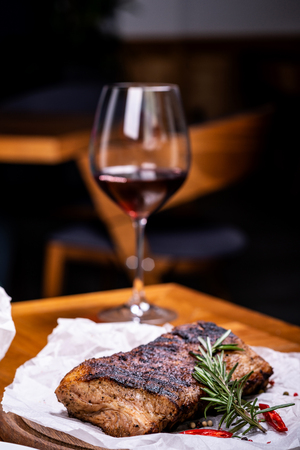 Striploin grilled beef steak served with rosemary, salt and peppercorns on wooden board with glass of wine.の写真素材