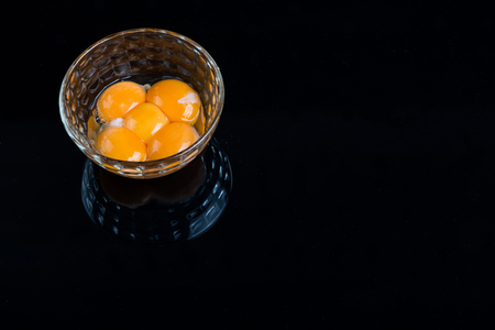 Bright yellow egg yolks in a glass bowl on black backgroundの写真素材