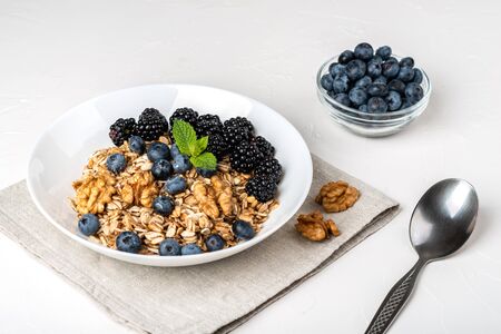 Healthy breakfast. Homemade granola, muesli, cereals with blackberries, blueberries, nuts, honey and mint in a white bowl on a white backgroundの写真素材