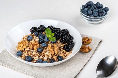 Healthy breakfast. Homemade granola, muesli, cereals with blackberries, blueberries, nuts, honey and mint in a white bowl on a white backgroundの写真素材