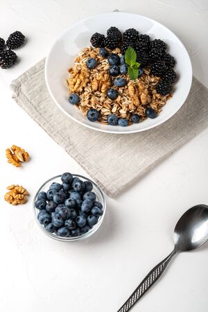 Healthy breakfast. Homemade granola, muesli, cereals with blackberries, blueberries, nuts, honey and mint in a white bowl on a white backgroundの写真素材