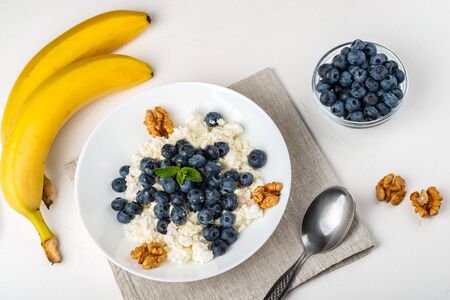 Healthy breakfast. Cottage cheese with blueberry, nuts, honey and mint in a white bowl on a white backgroundの写真素材