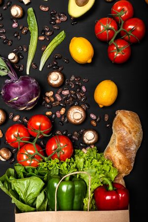 Different fresh vegetables and bread in shopping paper bag. Purchases concept. Healthy food organic selection on a black backgroundの写真素材