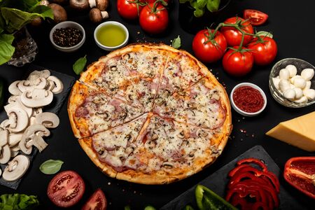 Homemade pizza ready to eat with raw ingredients. Top view on a black background.の写真素材