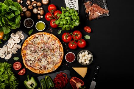 Homemade pizza ready to eat with raw ingredients. Top view on a black background.の写真素材