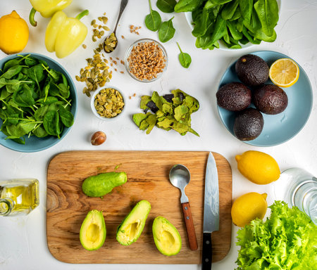 halves of avocado on a wooden board and other healthy diet ingredients on the kitchen table. Top...