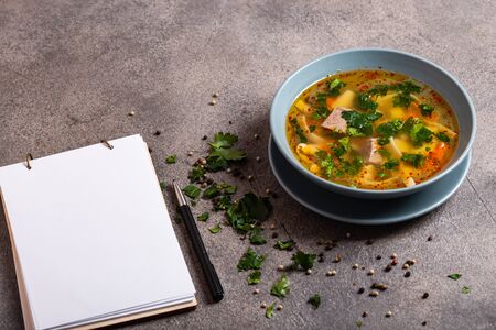 Delicious spicy soup with beef and noodle on grey background. A book for writing recipes lies on a table. Close-up.の写真素材
