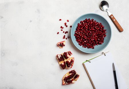 Grains of peeled pomegranate lie in a plate. Top view. Close-up. A book for writing recipes lies on the table. Copy space for textの写真素材