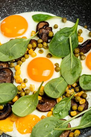 Homemade Fried eggs with mushrooms, green peas, corn and greens.の写真素材