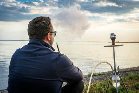 Man smoking hookah near the river at sunset