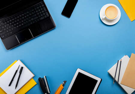 Online work or education concept. Laptop, tablet computer, smartphone, notepad, book, stationery on the blue background. Top view with copy space.の写真素材