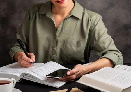Girl holds phone in hand, writes, study at home. Self education concept.の写真素材