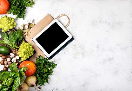 Online grocery shop concept. Tablet computer and shopping paper bag with different vegetables and greens. Top viewの写真素材