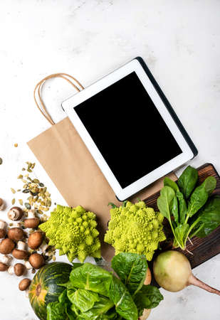 Tablet computer and shopping paper bag with vegetables and greens. Top viewの写真素材