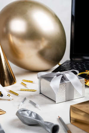 Online celebration concept. Silver festive box and laptop Balloon Other accessories on the white tableの写真素材