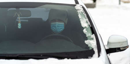 A man sits in a car wearing a virus-protective mask close-upの写真素材