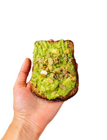 Avocado Guacamole Sandwich in a female hand with pumpkin seeds and wheat seedlings isolated backgroundの写真素材