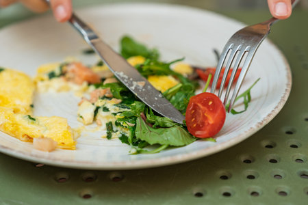 A persons hands cutting a fresh tomato while eating a delicious omelette for breakfastの写真素材