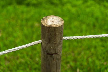 A close-up of a wooden post with a rope barrier on a blurred green grass backgroundの写真素材