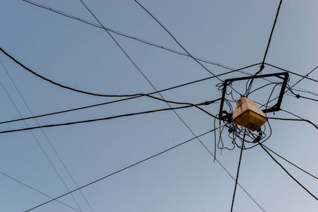 A chaotic tangle of electrical wires and cables with a street lamp against a clear evening sky