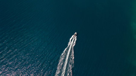 Top down drone of speedboat carving clean wake across teal sea near rocky coast minimal copyspace...