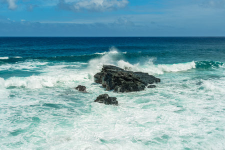 Massive turquoise ocean waves crashing dramatically against dark volcanic rocks off the coast of a tropical islandの写真素材