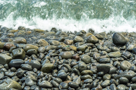 Wet round stones and pebbles of various sizes covering the entire beach surface, constantly washed...