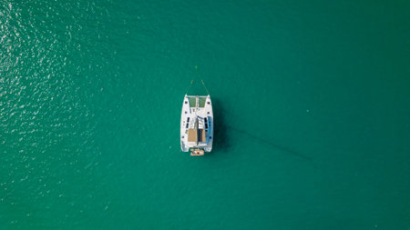 Top down drone view of white sailing catamaran anchored on turquoise lagoon minimal composition calm...